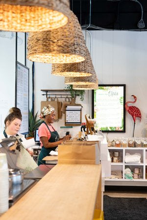 2 employées d'Olivia travaillant derrière le comptoir, préparant les commandes.