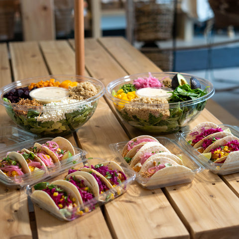 4 plateaux de tacos ainsi que 2 grandes salades traiteur placés sur une table de pic-nique